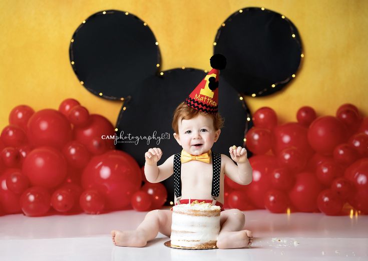 a baby sitting in front of a mickey mouse cake