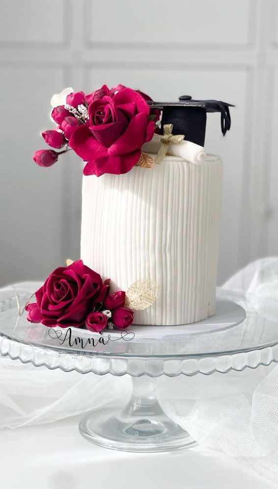 a white cake with pink flowers and a graduation cap on top is sitting on a glass plate