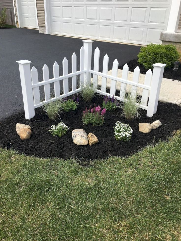 a white picket fence surrounded by black mulch and flowers in front of a house