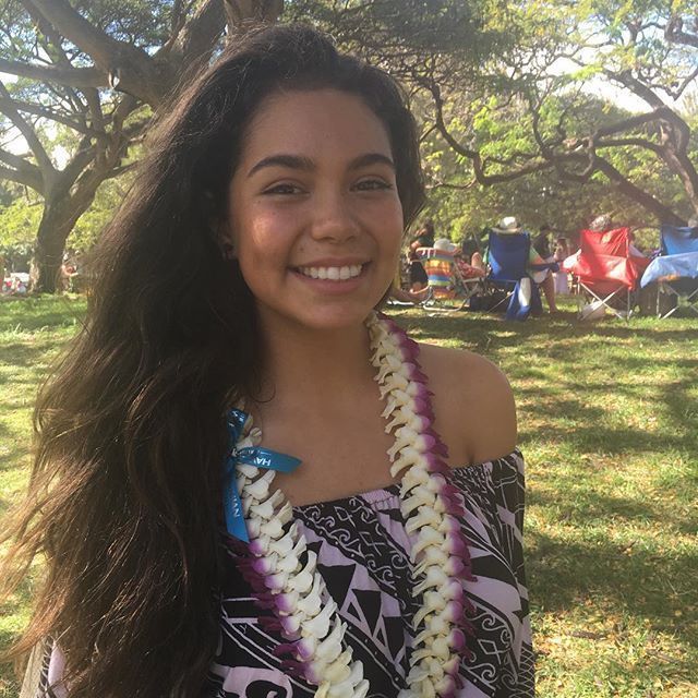 a woman with long hair wearing a lei and smiling at the camera in a park