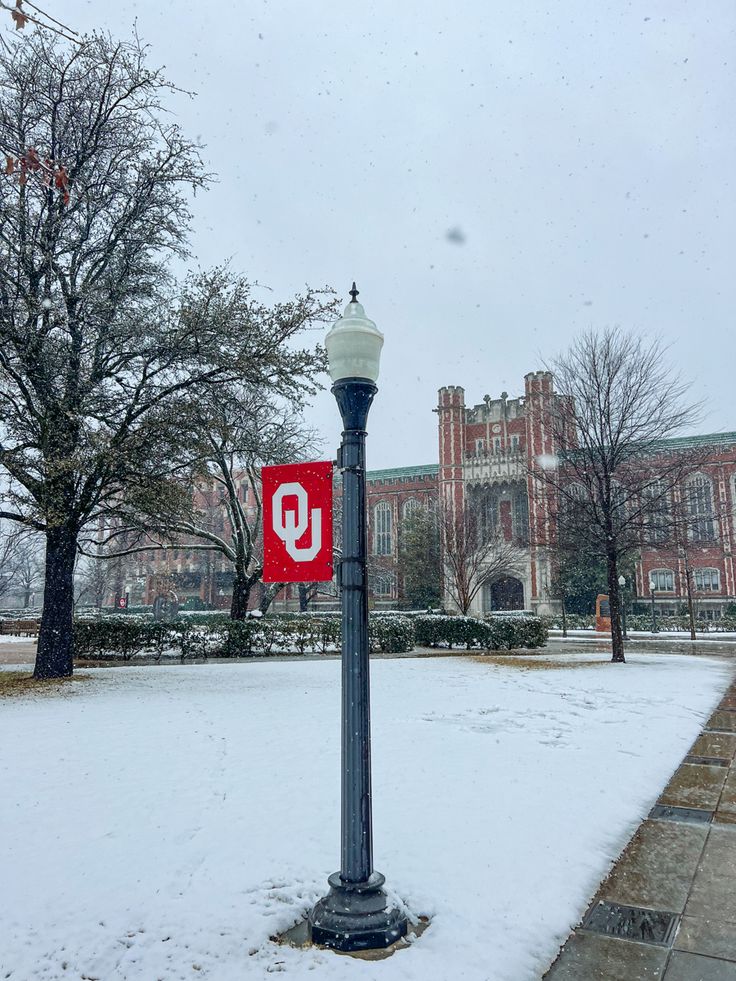 a lamp post with a red sign on it in front of a large building covered in snow