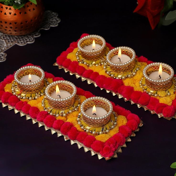 two decorative candles sitting on top of red and yellow cloth with gold trimmings