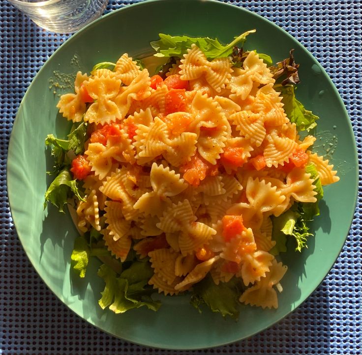 a green plate topped with pasta and lettuce next to a glass of water