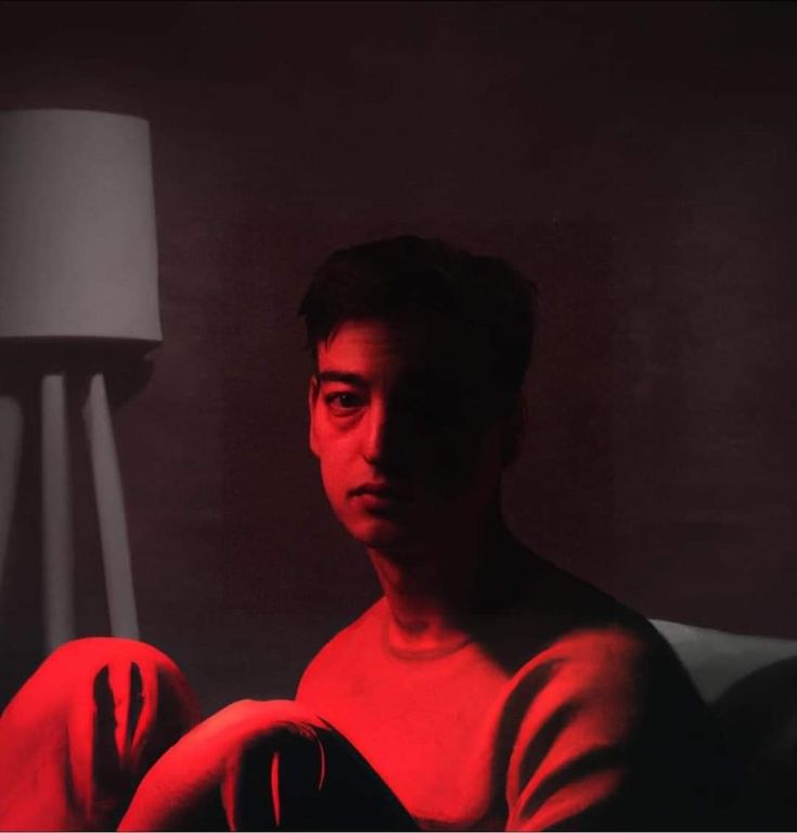 a man sitting on a couch in front of a lamp with red light coming from it