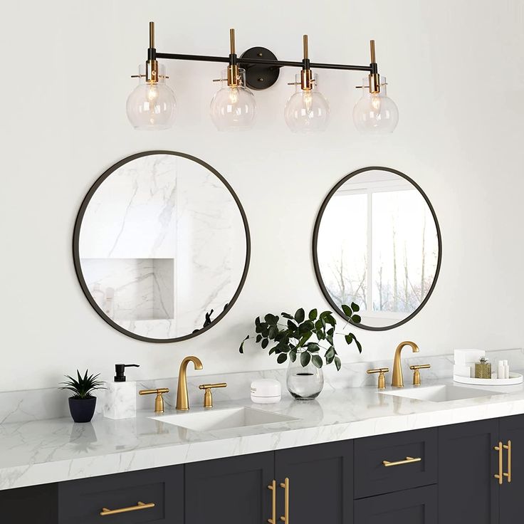 two round mirrors are above the double sinks in this bathroom with marble countertops and brass fixtures