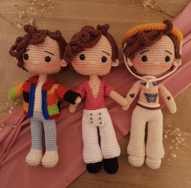 three crocheted dolls are standing next to each other on a pink cloth covered surface