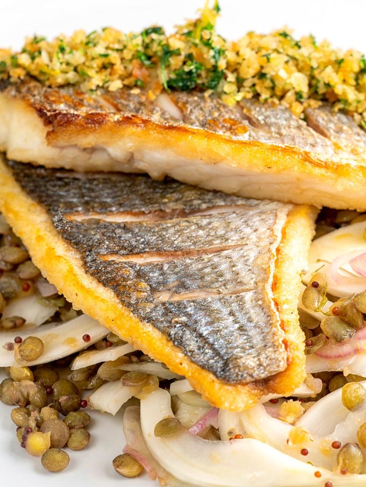 some kind of fish is sitting on top of some vegetables and beans in a white plate