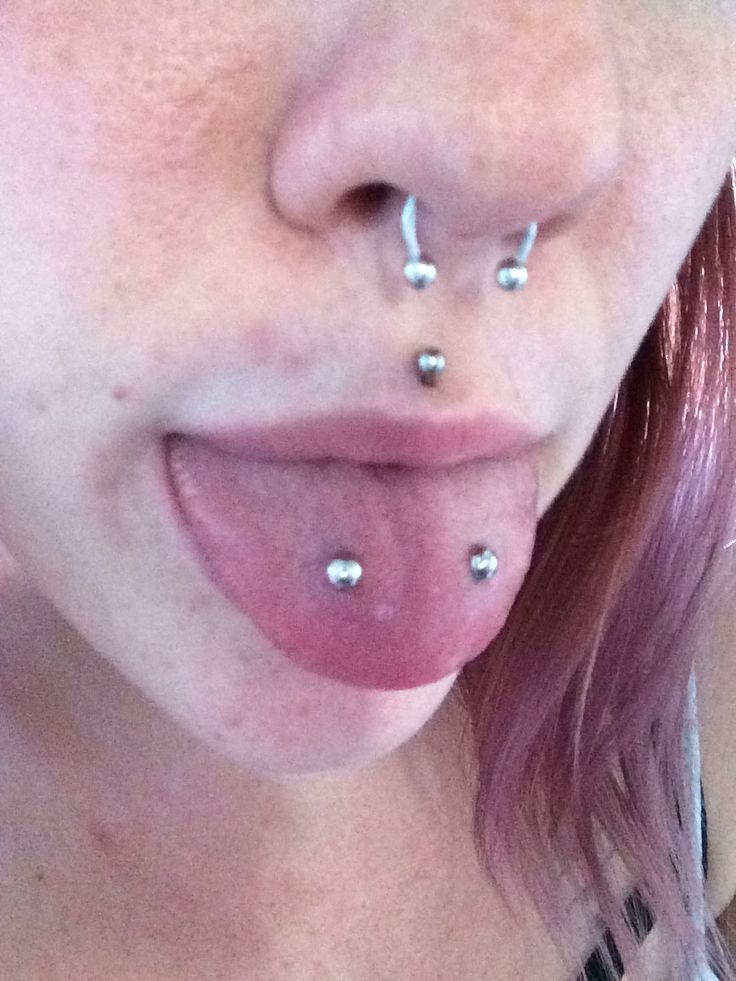 a close up of a person with piercings on her nose and tongue sticking out