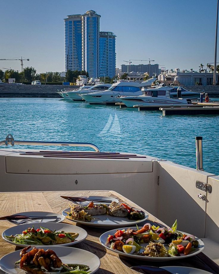 plates of food sit on the deck of a boat with boats in the water behind them