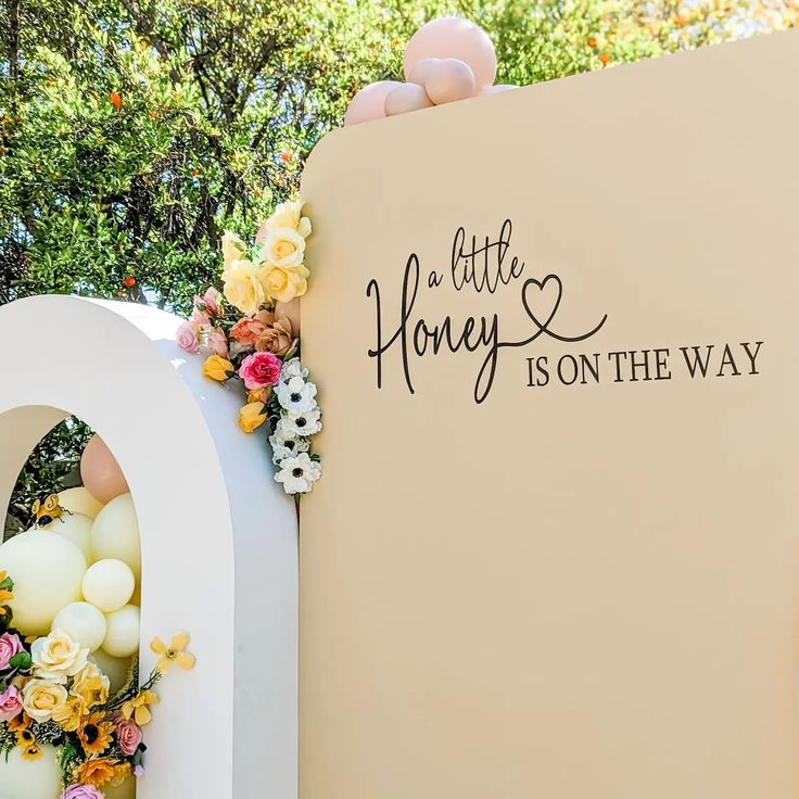 there is a sign that says little honey is on the way with flowers around it