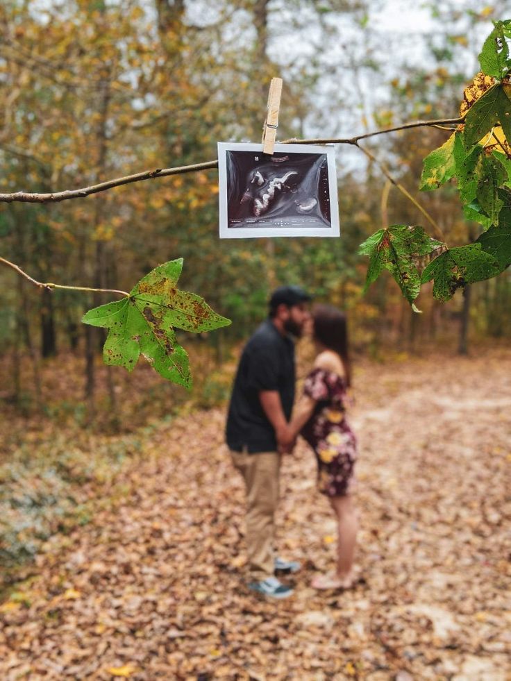 a man and woman standing next to each other on a leaf covered path in the woods