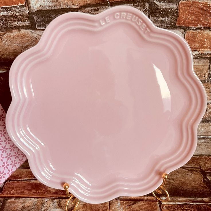 a pink plate sitting on top of a wooden table next to a brick wall and napkins