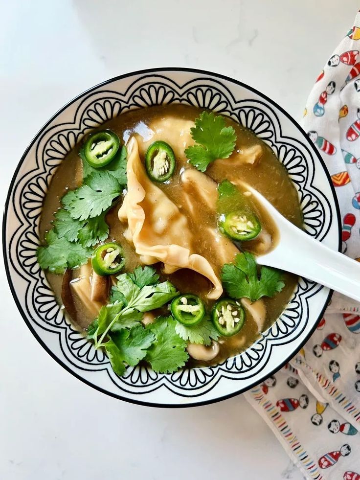 a person is holding a spoon over a bowl of soup with noodles and green peppers