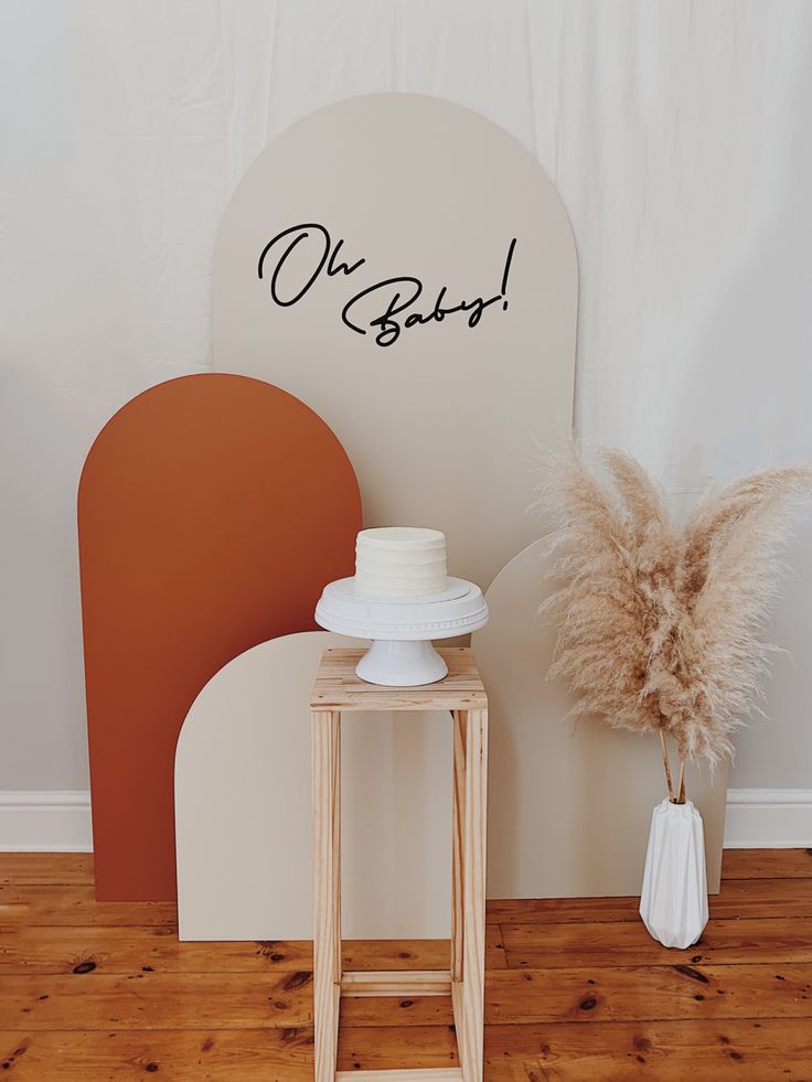 a cake sitting on top of a wooden table next to a white vase with dry grass