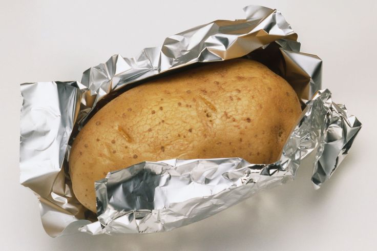 a baked potato in aluminum foil on a white surface