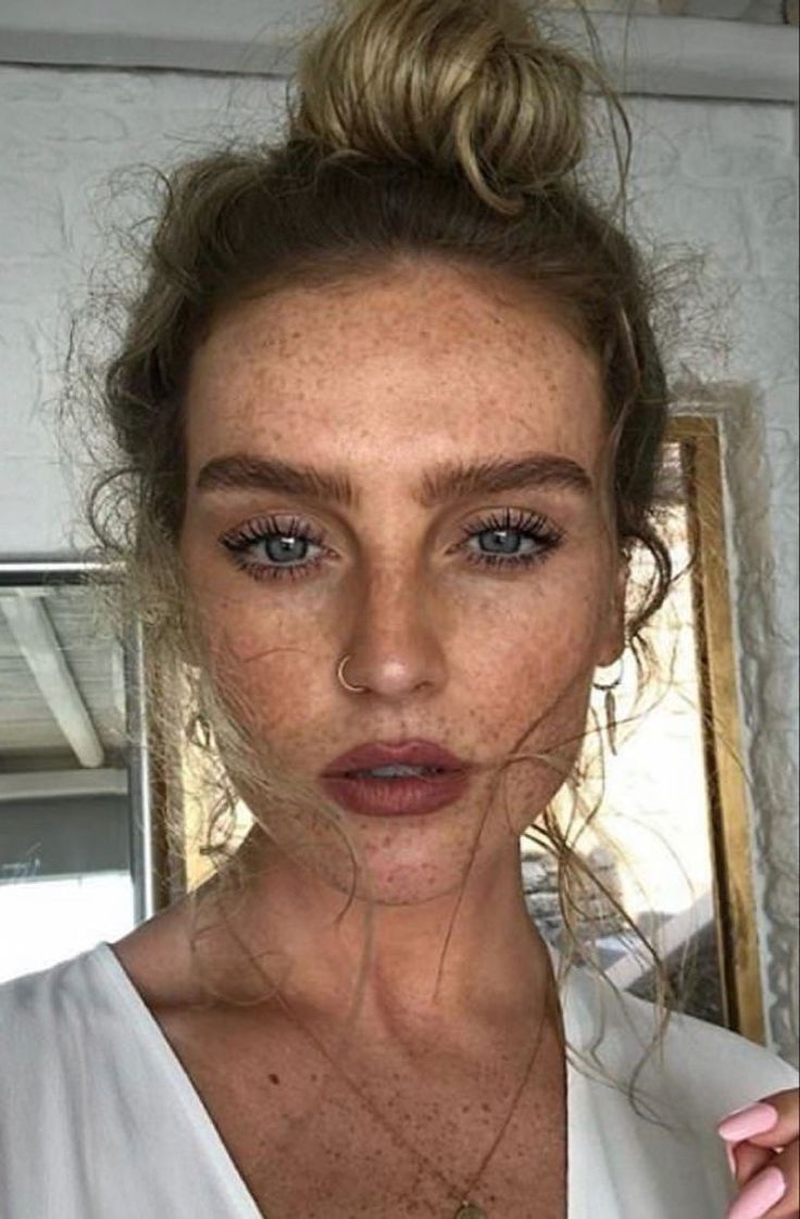 a woman with freckled hair and blue eyes looks at the camera while wearing a white top