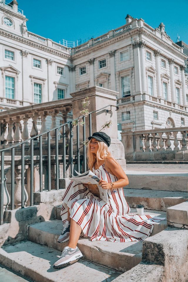 a woman sitting on steps in front of a building wearing a hat and striped dress