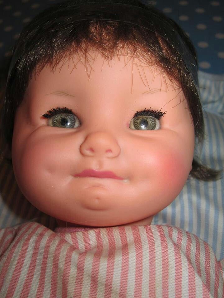 an old doll with big eyes laying on a bed and looking at the camera while wearing a striped shirt