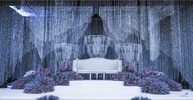 a white bench sitting in front of a window covered in curtains and purple flowers on the ground