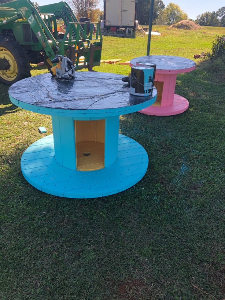 two tables made out of concrete sitting on top of a green field next to a tractor