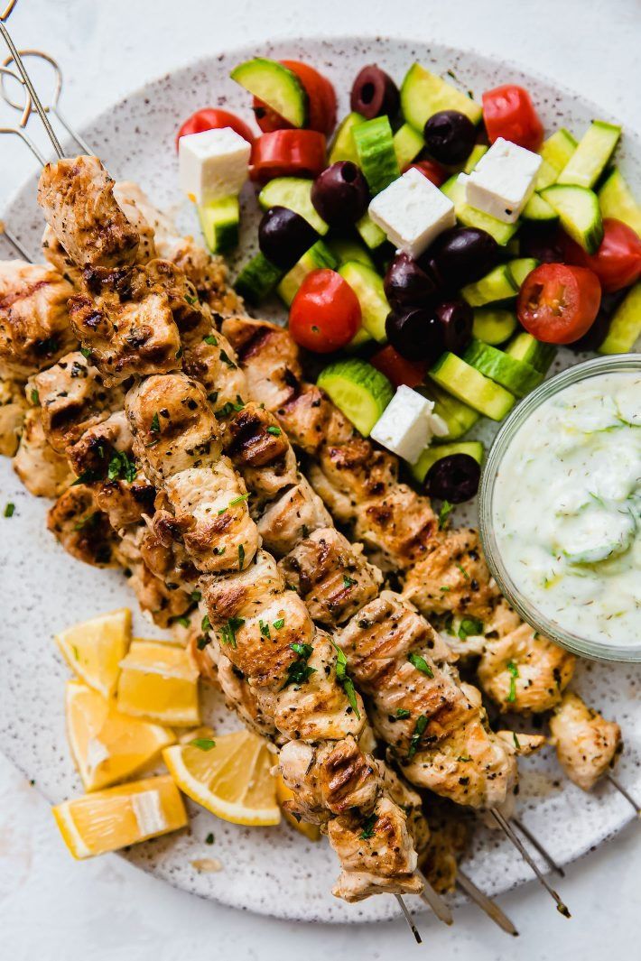 chicken kabobs with cucumber, olives, and tzatzh on a white plate