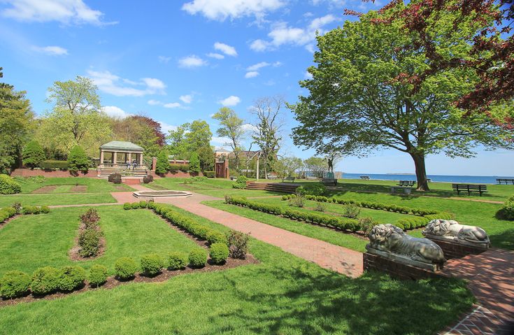 a large garden with many plants and trees near the water in front of a gazebo