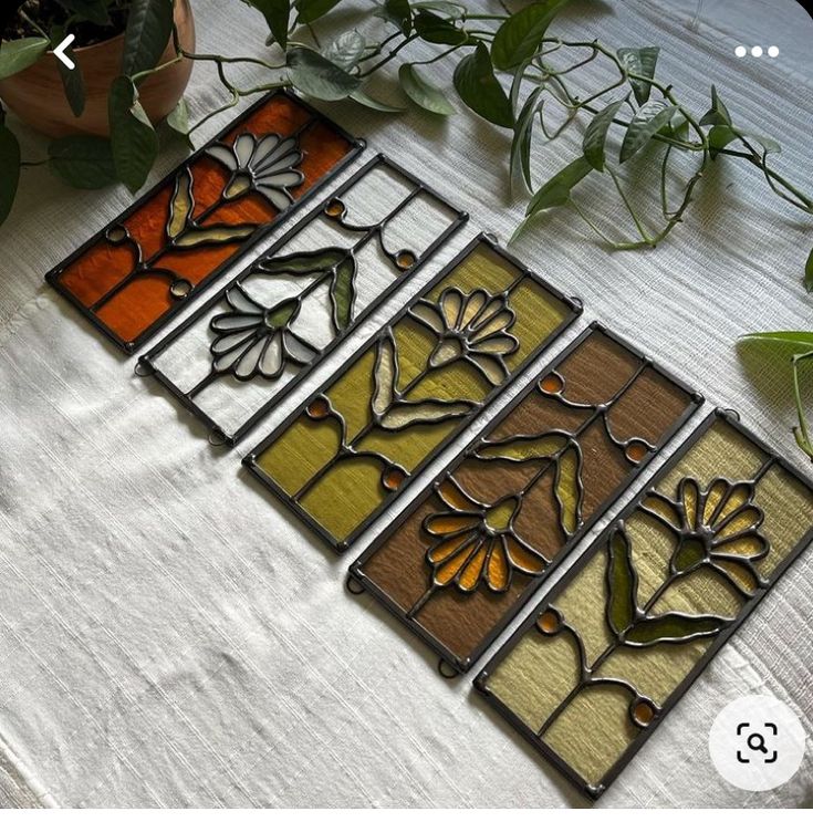 four stained glass panels sitting on top of a table next to flowers and leaves in vases