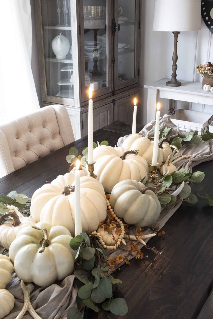 a dining room table with white pumpkins and greenery on the centerpiece, candles in front of it