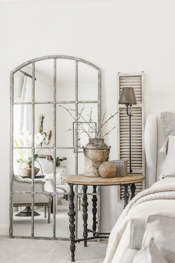 a mirror sitting on top of a bed next to a table with flowers in it