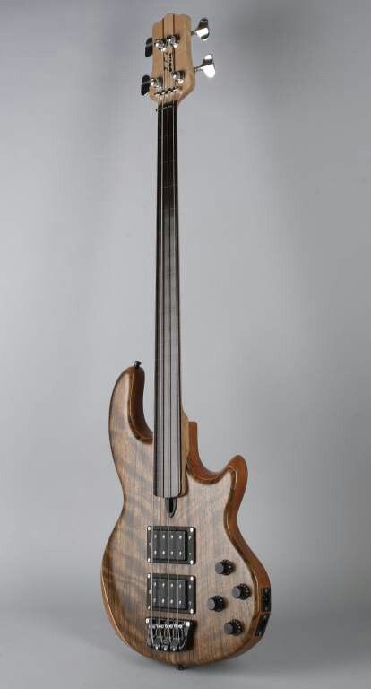 an electric bass guitar sitting on top of a gray surface with its head turned to the side