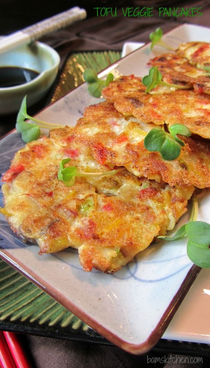 three vegetable pancakes on a plate with chopsticks and sauce in the back ground