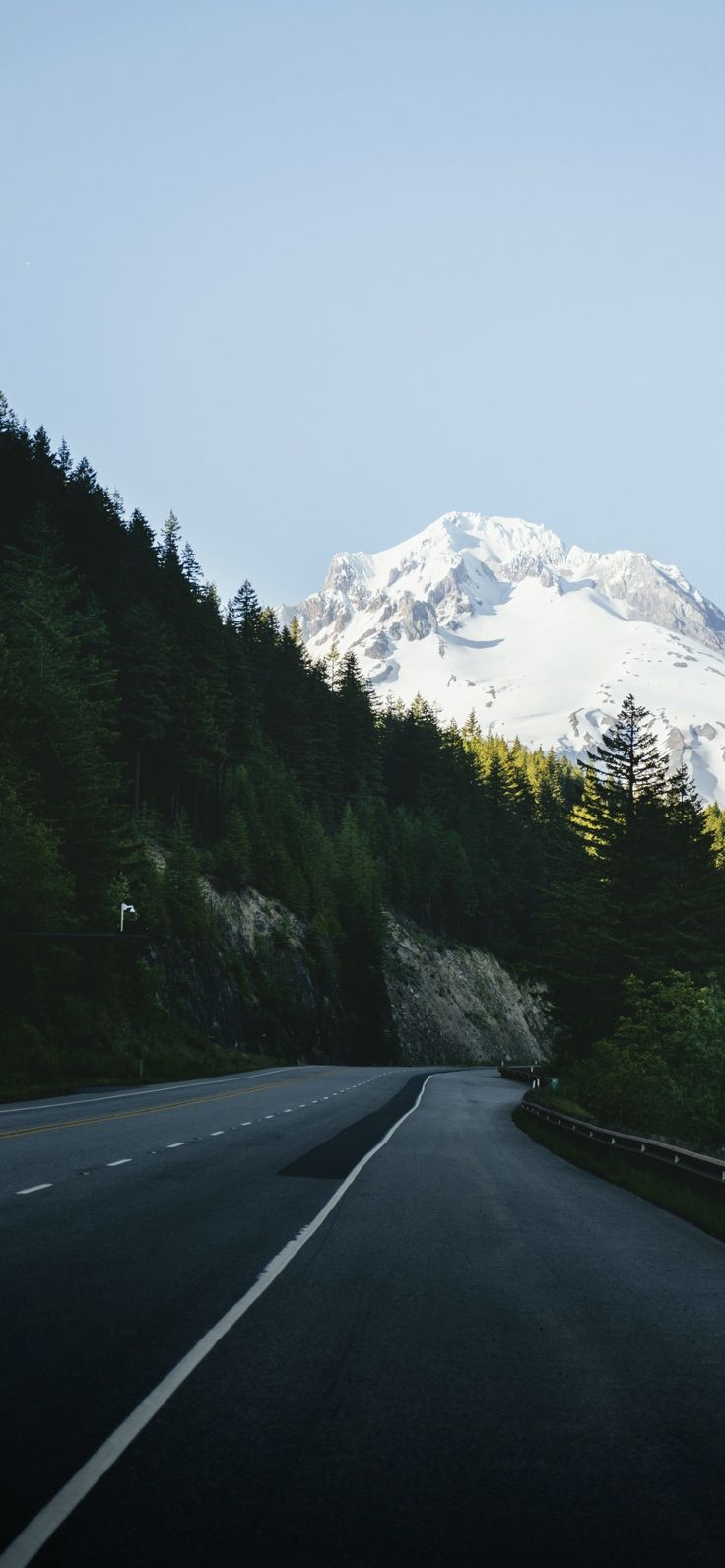 an empty road in front of a snow covered mountain with pine trees on both sides