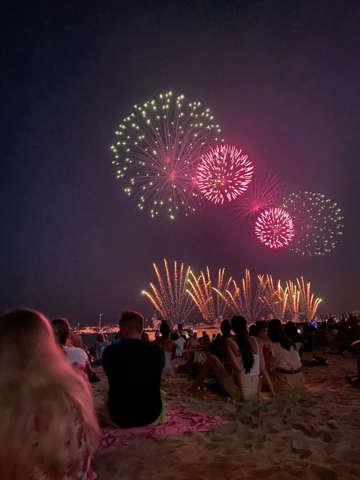 people are sitting on the beach watching fireworks