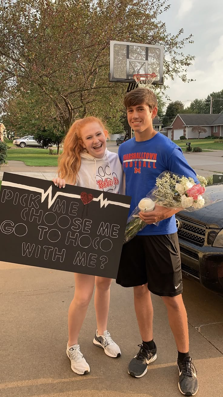 two people standing next to each other holding flowers and a sign