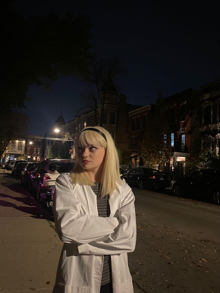 a woman standing in the street at night with her arms crossed and looking off to the side