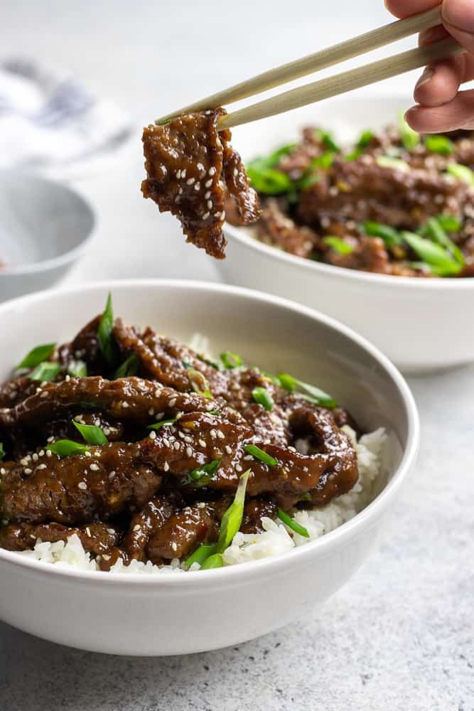 someone is holding chopsticks over a bowl of beef and rice with green onions