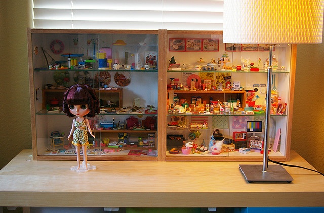 a doll is standing in front of a shelf full of dolls and other items on the table