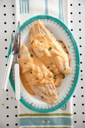 a white plate topped with chicken covered in gravy next to a fork and knife