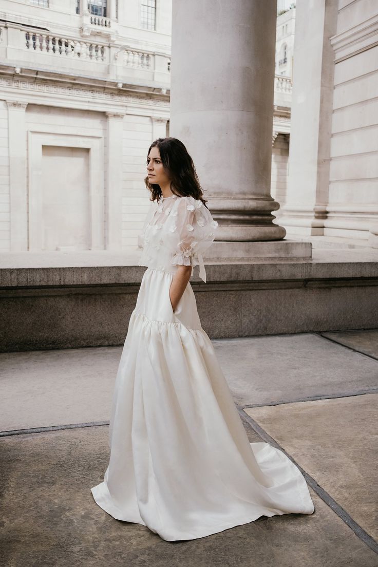 a woman in a white dress is standing on the sidewalk near some pillars and columns