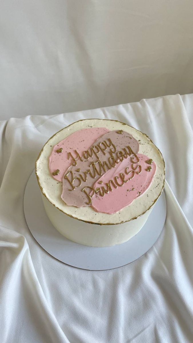 a birthday cake with pink frosting on a white tableclothed surface, in the shape of a circle