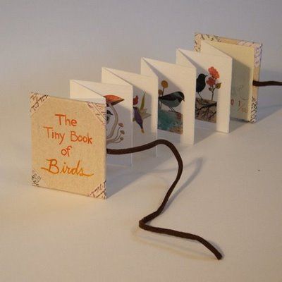 the tiny book of birds is being held up by a brown string and two small cards are in front of it