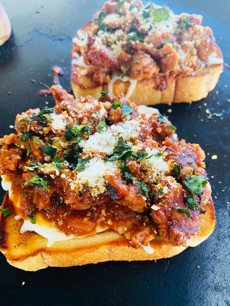 two pieces of bread with meat and cheese on them sitting on a black counter top