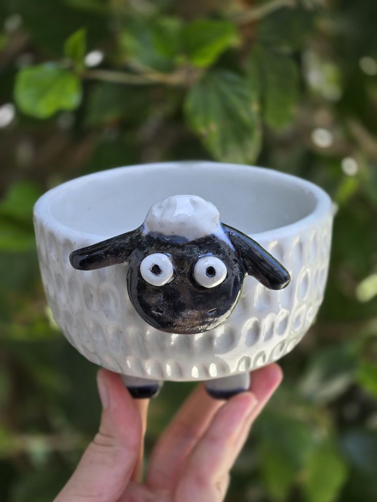 a hand holding up a white bowl with a black sheep on it's face