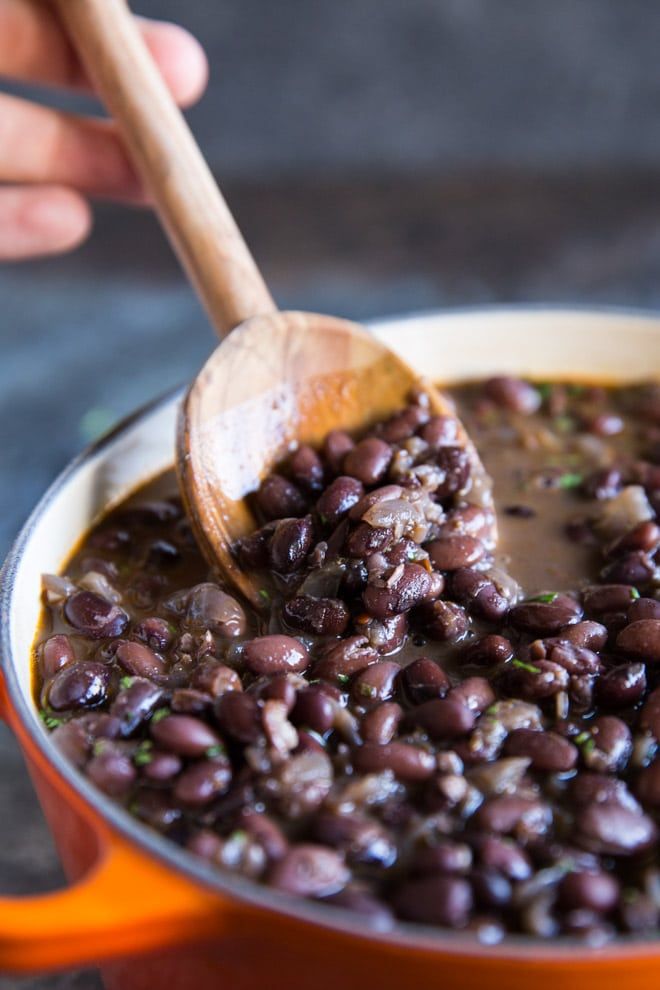 a pot full of beans with a wooden spoon in it and someone's hand