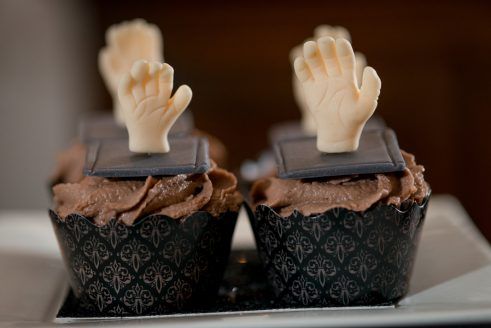 two cupcakes with chocolate frosting and hands sticking out of the icing