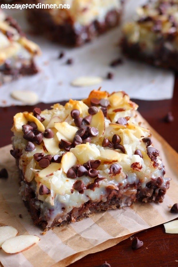 a piece of cake sitting on top of a wooden cutting board with chocolate chips and almonds