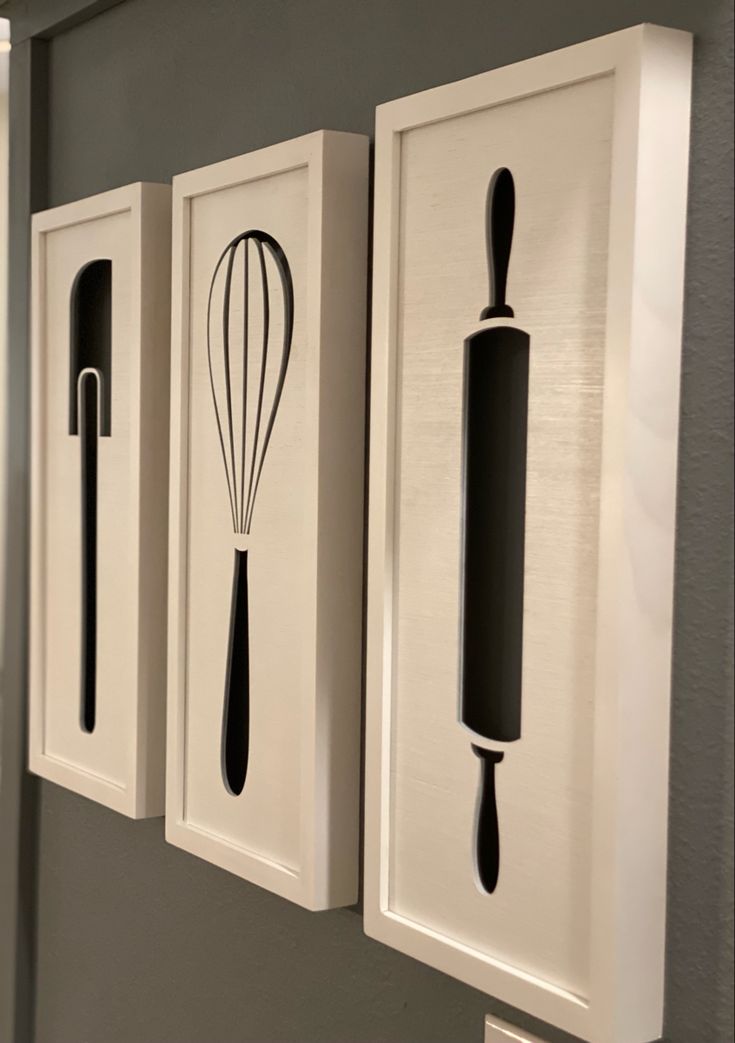 three kitchen utensils are hanging on the wall next to two framed pictures with one whisk in it