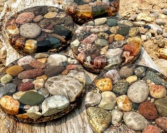 four plates with rocks on them sitting on a wooden table in the sand and water