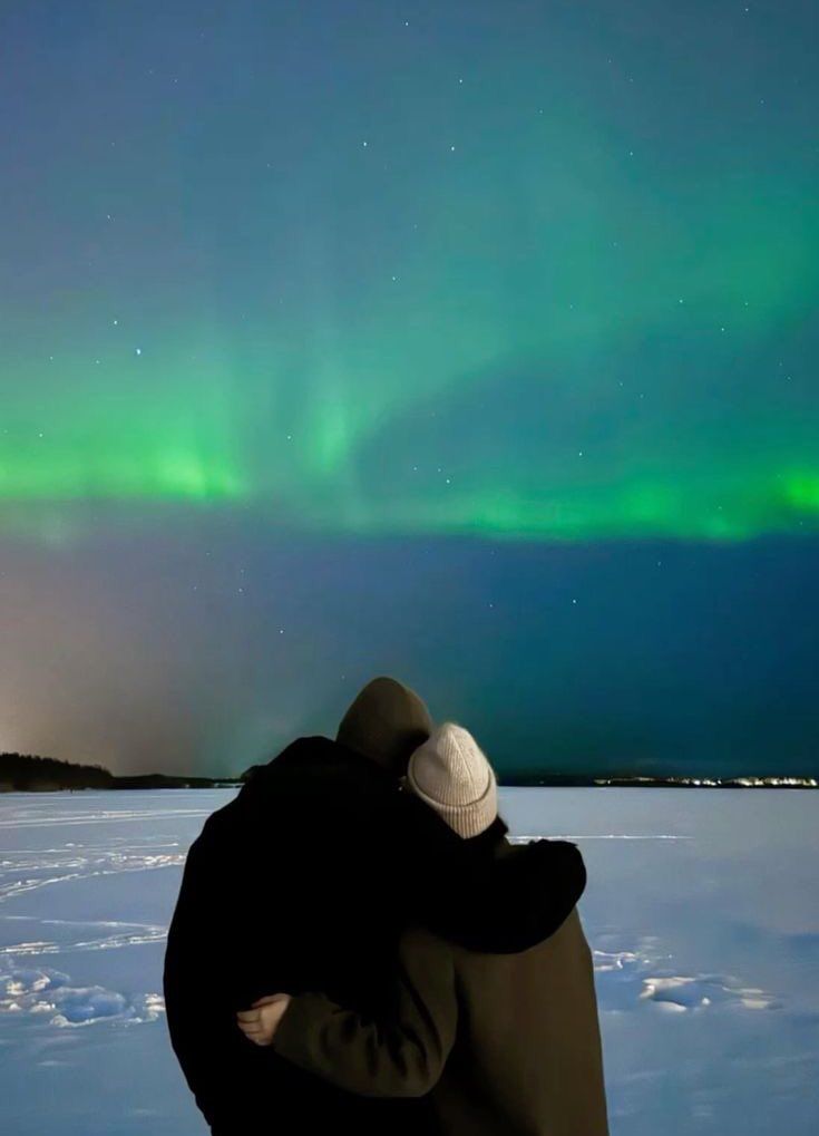 a man standing in the snow looking at an aurora bore above him and his back to the camera