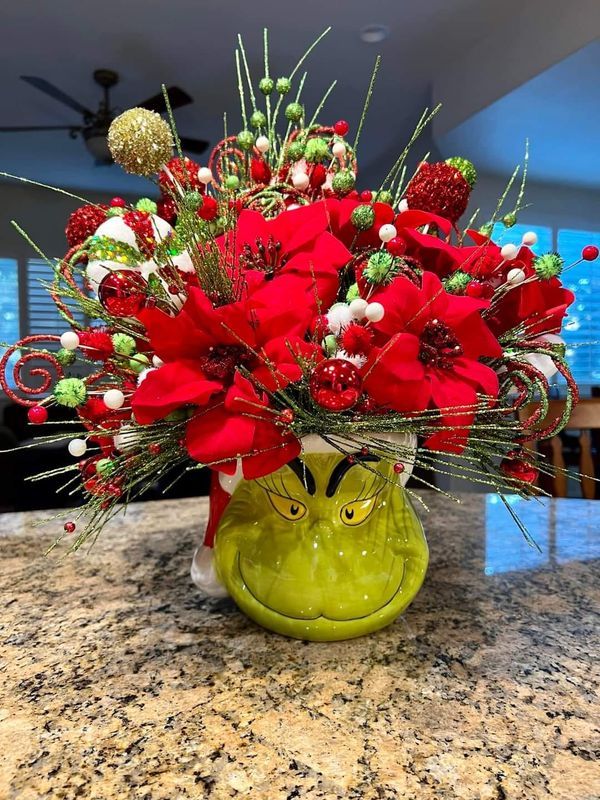 a green vase filled with red flowers on top of a counter